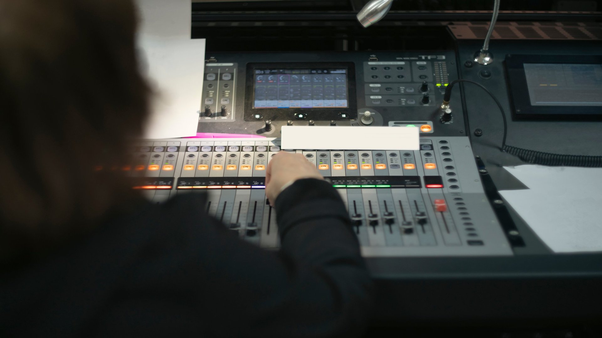 Professional audio engineer operating a digital soundboard in a dark studio with illuminated faders