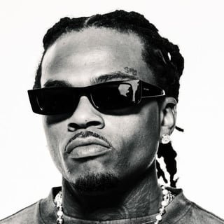 Black and white portrait of a man wearing dark sunglasses, a braided hairstyle, and a beaded chain necklace
