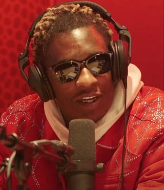 Person wearing sunglasses and red sparkly jacket speaking into microphone with headphones against red background