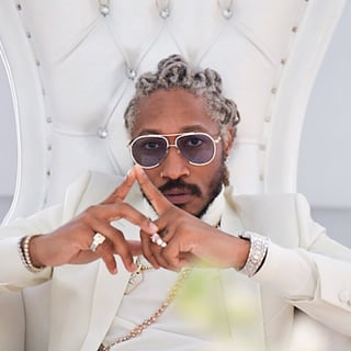 Man in white suit and oval sunglasses posing in modern white chair with hands crossed